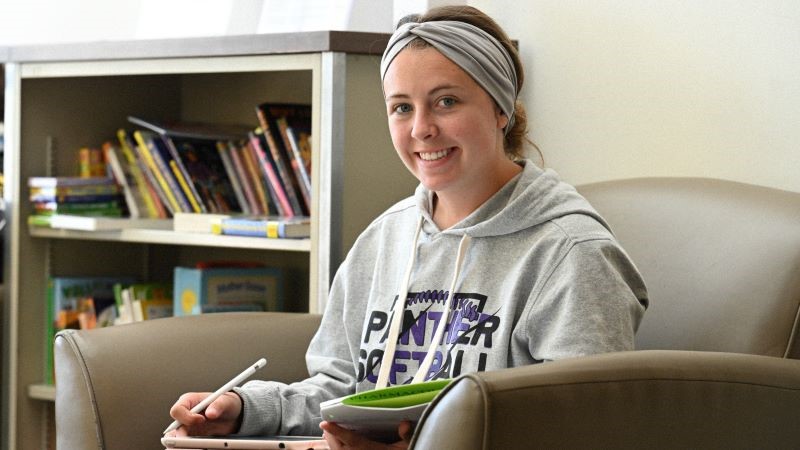 Student Reygan Carlile studying by a bookcase