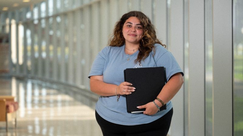 Indoor candid of a student holding a binder in glass hallway